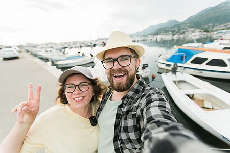 在夏季港渡船码头的智能手机室外 与船只和游艇近距离拍摄摄影机时笑着自画肖像的年轻夫妇照片码头拥抱城市夫妻旅游假期港口博主女性图片