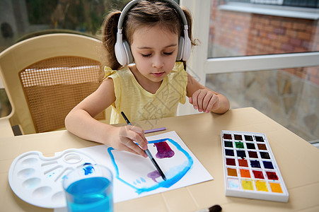 戴耳机的可爱学龄前女孩 小艺术家画画 用水彩颜料 爱好 美术大师班图片