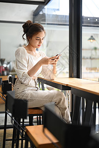 美丽的年轻女子在咖啡店旁看社交媒体或上网聊天时用智能电话聊天 她坐在咖啡厅里背景
