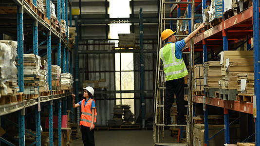 安全管理仓库内雇员身戴硬帽子和反射夹克 在仓库的货架上包装包裹背景