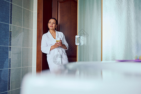 穿着白色浴袍 自信 漂亮 可爱的女人 站在舒适的家庭浴室里 手里拿着一杯柠檬水图片