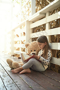 她们都沉浸在一个好故事里 一个小女孩在看书 带着她的泰迪熊陪着她图片