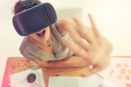 完全沉浸在数字世界中 惊叹不已 一位年轻女商务人士在办公室工作时戴着 VR 耳机的高角度镜头图片