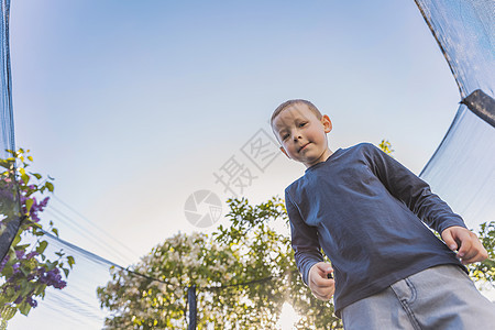 男孩在蹦床上跳跃微笑运动玩具金发女郎童年男生幸福乐趣热情天空图片
