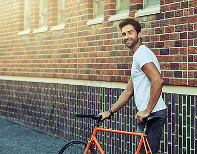 一个英俊的年轻男子在城里度过一天 生活于城市中 他喜欢现代方式姿势男人城市成人微笑自行车胡须休闲装潮人裁剪图片