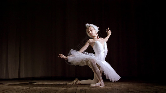 在聚光灯下 在旧剧院大厅的舞台上 穿着白天鹅和足尖鞋的年轻芭蕾舞演员 优雅地跳着某种芭蕾舞动作 部分是胸罩舞蹈训练成人运动女孩姿图片