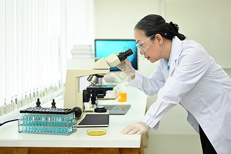 高级女性生物技术专家在显微镜下观察 在实验室进行实验图片