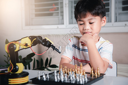 亚洲小男孩思考和等待机器人臂象棋游戏的亚洲男孩机器人桌子电子产品作坊童年孩子科学工程师技术学校图片