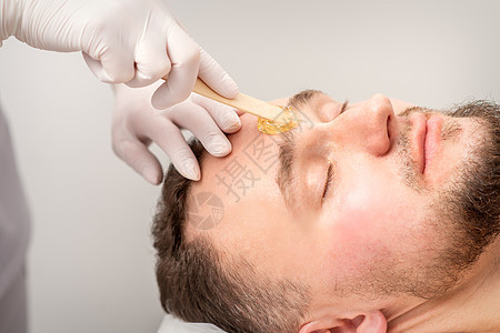 美容师在美容院做蜡时 在眉毛之间涂蜡糊 笑声治疗皮肤前额卫生服务男性美容化妆师药品头发图片
