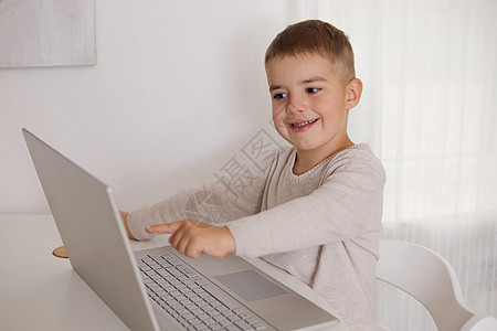 木板上的孩子快乐的小男孩在家里的笔记本电脑上玩游戏 一个孩子在家里用电脑看卡通片的画像 现代儿童和教育技术闲暇学习游戏互联网童年长椅屏幕白色背景