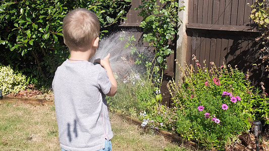 有趣的小男孩在花园房屋后院浇灌草坪植物 可爱的孩子在炎热的阳光明媚的夏天在户外玩灌溉软管 孩子们帮忙做家务 孩子们的活动 童年花图片