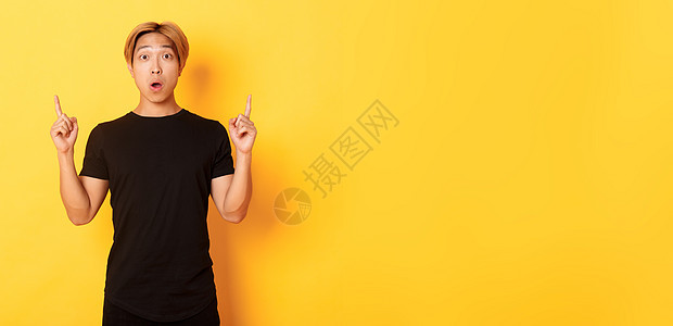 穿着黑色T恤 张嘴着迷 举起手指 黄色背景的令人惊讶的亚洲人肖像快乐教育广告工作室职业男朋友发型成人学生购物图片