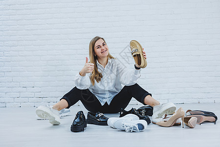 一位年轻女子坐在地板上的鞋子中间 为自己挑选新鞋 穿白衬衫和黑裤子的女士 穿白鞋的女人衣架地面鞋类内阁派对运动运动鞋店铺裙子女性图片