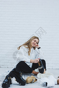 一位年轻女子坐在地板上的鞋子中间 为自己挑选新鞋 穿白衬衫和黑裤子的女士 穿白鞋的女人魅力女孩运动零售鞋类房间派对运动鞋衣柜店铺图片