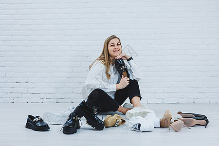 一位年轻女子坐在地板上的鞋子中间 为自己挑选新鞋 穿白衬衫和黑裤子的女士 穿白鞋的女人裙子鞋类脚跟女孩商业衣架运动鞋零售地面派对图片