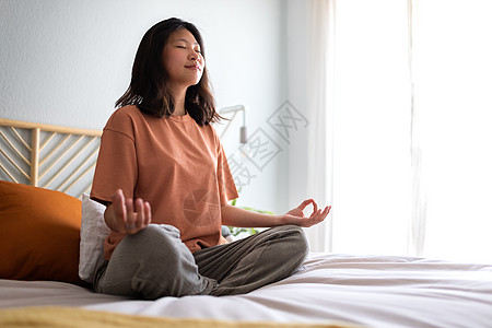 年轻的亚洲女人穿着舒适的衣服 早上在床上冥想以清除脑海 复制空间 (笑声)图片