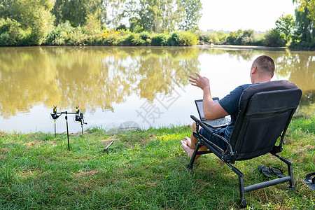 一名男子坐在秋湖附近的椅子上 从事笔记本电脑自由职业露营工作 机器人走出办公室 与同事通电话背景图片