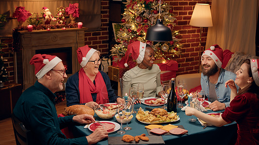 欢快欢笑的多民族家庭在晚餐时唱着圣诞歌曲 一边喝着起泡酒图片