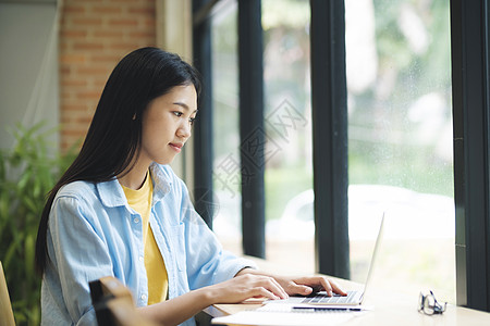 年轻的亚洲妇女使用笔记本电脑学习 坐在桌子上图片