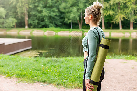 湖边瑜伽夏天在公园里的一个苗头女人 在她身后有个绿色的健身垫子背景