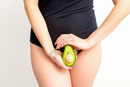 健康营养和怀孕概念 年轻女性在白色背景中 将一半的鳄梨水果放在靠近其腹部的腹部附近母亲子宫生育力肚子女士工作室生活饮食分娩产科图片