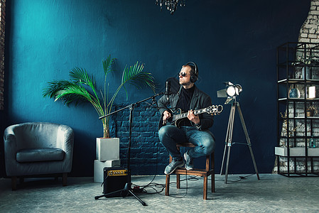 男歌手坐在凳子上 戴着耳机 吉他在家庭录音室录制曲目生产流行音乐卡拉ok电缆创造力嗓音独创性工作室扬声器记录图片