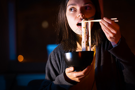 女孩在笔记本电脑上吃面和看录像桌子女士拉面技术商务职场人士工作电影失眠图片