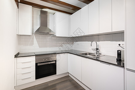 经典风格的现代轻型厨房 配有白色木质角柜 光滑的深色大理石台面和白色墙砖 厨房用具和配件由不锈钢制成图片
