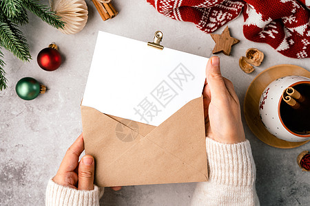 女人手里拿着白纸和信封的毛衣 平躺的灰色背景与一杯咖啡和圣诞装饰 顶视图模拟和复制文本空间图片