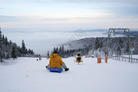 在德国黑森州 Ren 的山上 一名男子在壮丽的冬季景观背景下骑着雪橇 神奇的高大苍松和雪杉覆盖着冰雪 地平线创造了一种幻觉 并与图片