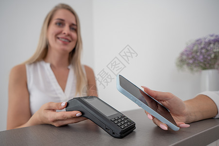妇女使用智能手机使用的NFC非接触付款支付费用通信零售客户出纳员沙龙柜台电子商务扫描商品账单图片