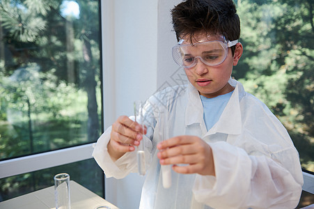 穿着白色实验室外套的青少年男学生拿着带化学实验室的试管 孩子和科学概念图片