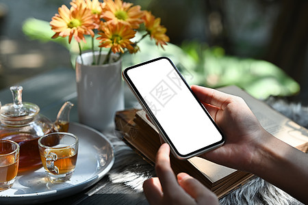 手拿着智能手机与传统茶具 杯子和茶壶放在质朴的木桌上 特写视图图片