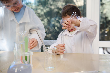 木板上的孩子在学校实验室的化学课上 把注意力集中在小女孩的手上 用化学品将试剂倒入试管中背景
