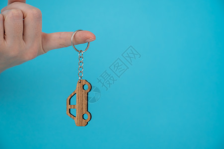 女人的手握着木钥匙链 车形是蓝色背景的汽车生态价格钥匙圈手指车辆礼物女性展示交易商业图片