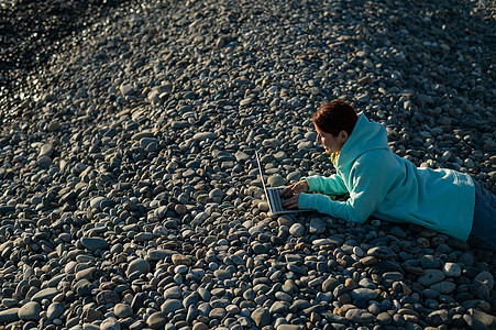 白种女人躺在卵石沙滩上的肚子上 打笔记本电脑 远距离工作自由职业者阳光海岸海滩互联网太阳石头旅行日出学生荒野图片