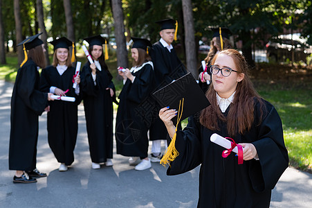 一名戴眼镜和毕业礼服的黑人年轻女子在同学背景下被画成肖像 一群研究生户外活动 见ECN 4Sub 220016 附件青少年学士朋图片