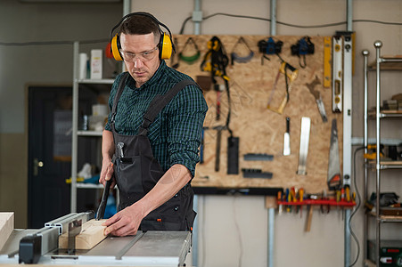 耳机包装男人在锯锯机上砍木板承包商技术员爱好维修建设者工作耳机工艺木工拼图背景