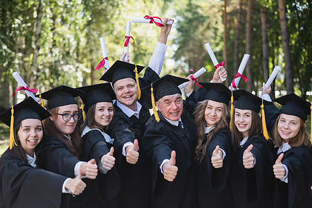 一群穿着长袍的毕业生在户外举起拇指快乐成就教育友谊微笑成人校园大学朋友们证书图片