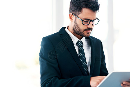 如今 商务人士使用应用程序做事 一个英俊的年轻商务人士站在现代办公室里使用数字平板电脑图片
