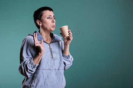 棕褐色模型的肖像 拿着一杯咖啡喝着热辣卡布奇诺咖啡杯 在烧掉她的舌头后作负面表情图片
