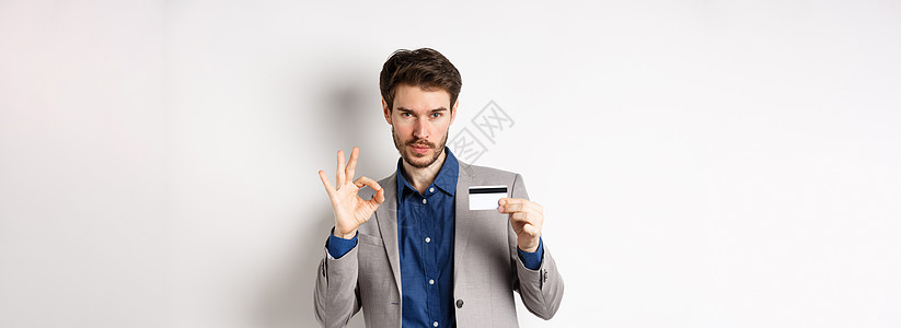 快乐的男性银行客户在商业西装中展示塑料信用卡和好牌 微笑满意 站在白背景上站立库存套装工作室购物成功胡须办公室情绪生活商务图片
