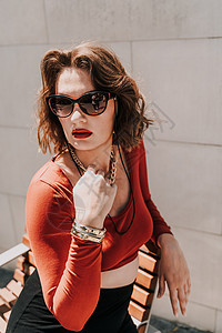 一个女人在街上的画像 外面的长凳上坐着一个戴着眼镜 穿着红色衬衫和黑色裙子的迷人女人绿色身体街道成人人行道城市头发连衣裙卷曲微笑图片