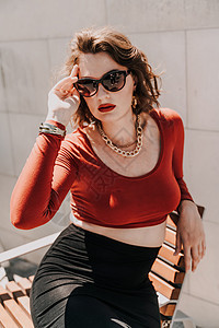 一个女人在街上的画像 外面的长凳上坐着一个戴着眼镜 穿着红色衬衫和黑色裙子的迷人女人街道身体姿势冒充头发女性腰带城市条纹连衣裙图片