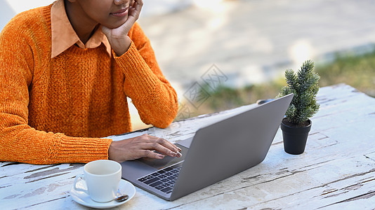 非洲青年妇女在户外咖啡厅休息 用笔记本电脑在木制桌子上使用图片