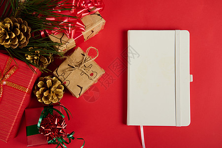 平面贴白纸条 圣诞礼物盒旁边的议程书和金松果 红底幕 复制广告空间图片
