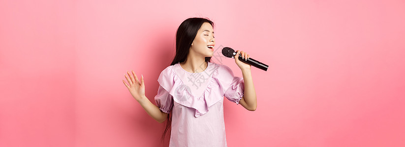 美丽的亚洲女孩表演歌唱 用麦克风唱歌 笑笑浪漫 穿着衣服站在粉红背景上 Y 我歌手化妆品青少年工作室投标女士购物女性情感卡拉ok图片