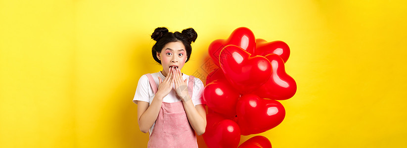 突然感到惊讶的韩国女孩喘气说哇 看在情人节特别宣传报价 站在大红心气球和黄色背景旁边 笑声热情女士假期促销微笑情感惊喜震惊展示工图片