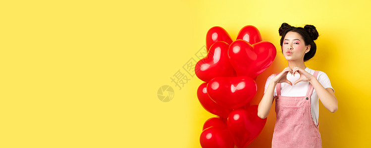 美丽的亚洲女人展示了心意 我爱你的手势和亲吻嘴唇 站在浪漫的红色气球旁边 情人节的概念周年化妆品惊喜女孩投标女士男朋友女朋友工作图片