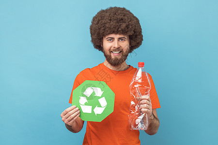 手持绿色标志和塑料瓶的微笑者看着相机 拿着回收剂图片